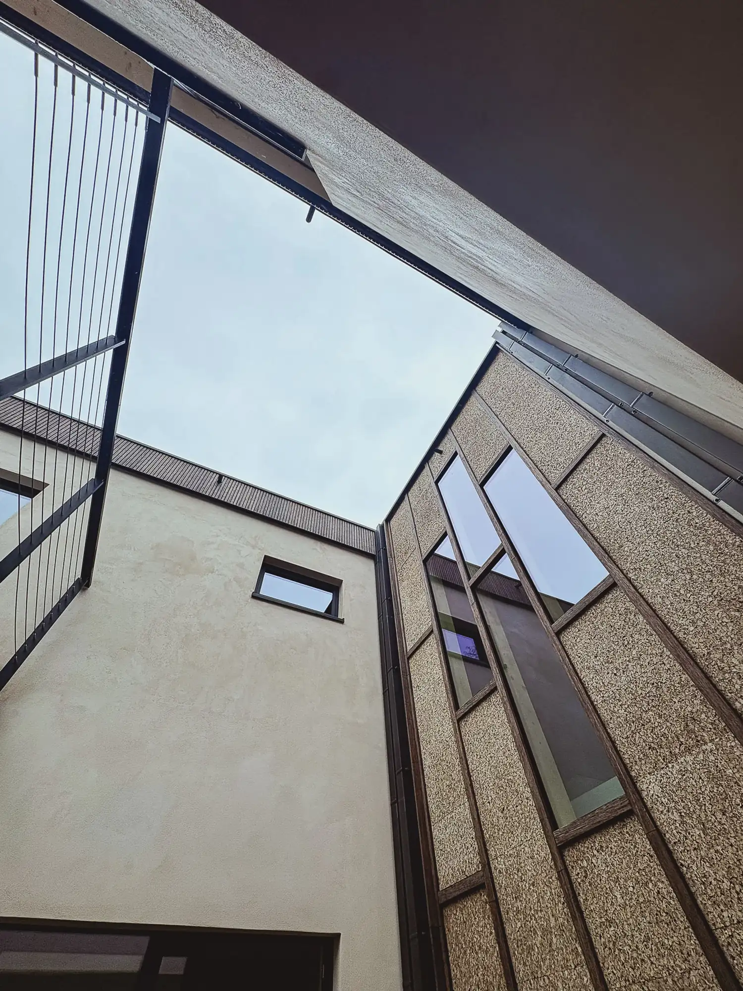 Contre-plongée dans un angle du bâtiment : enduit à la chaux clair d'un côté, panneaux de liège expansé de l'autre