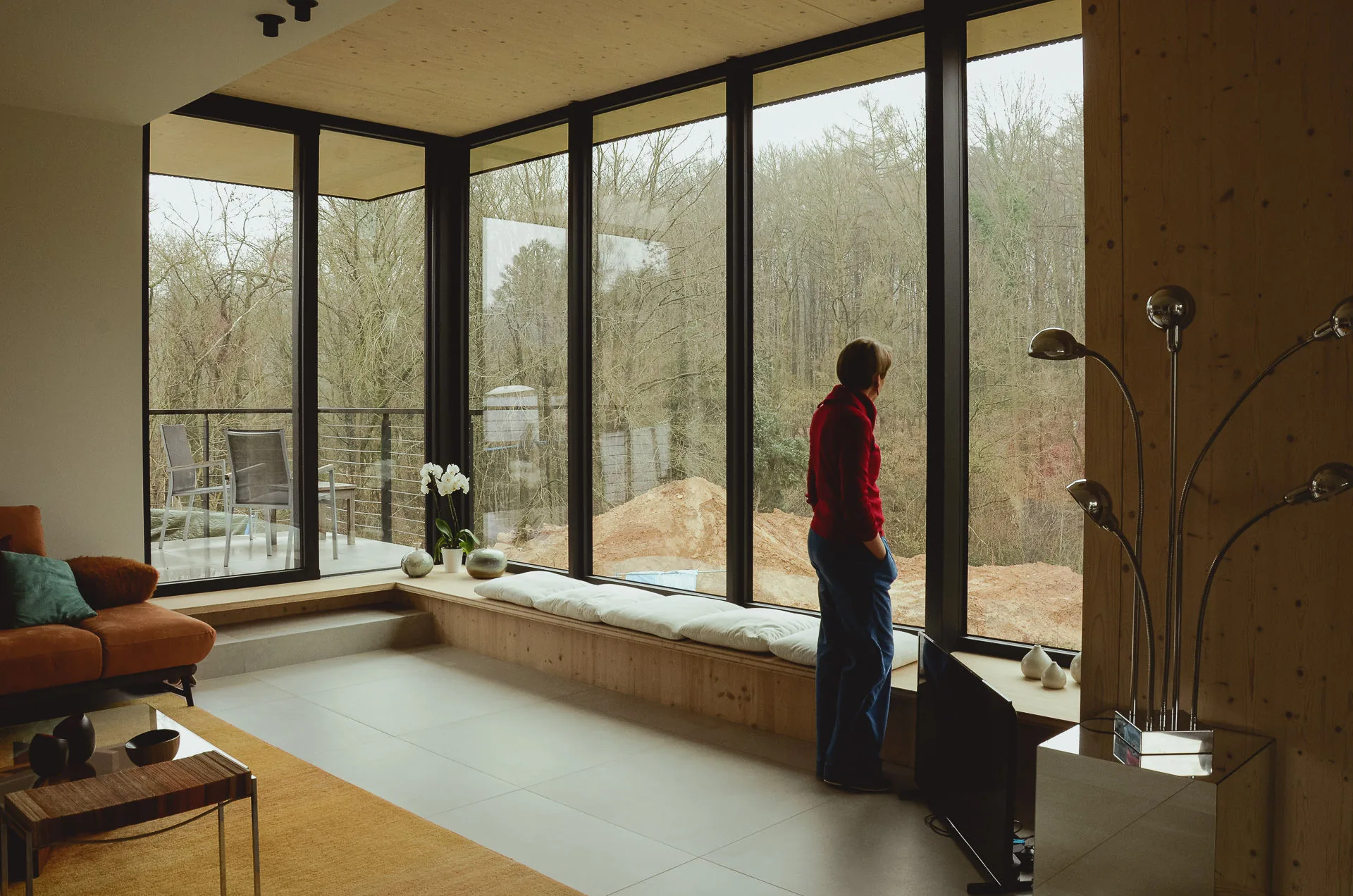 Le séjour ouvert sur la forêt par une baie d'angle, plafond et poteau en CLT apparent, banquette en allège