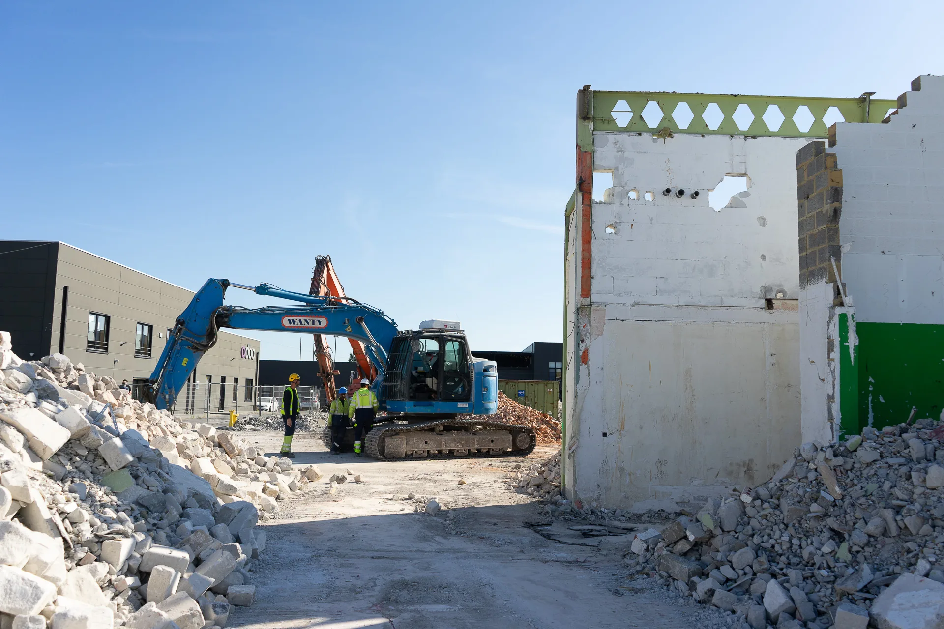 Démolition sur le campus Odoo : une pelleteuse entre deux tas de gravats, un pan de l'ancien bâtiment encore debout