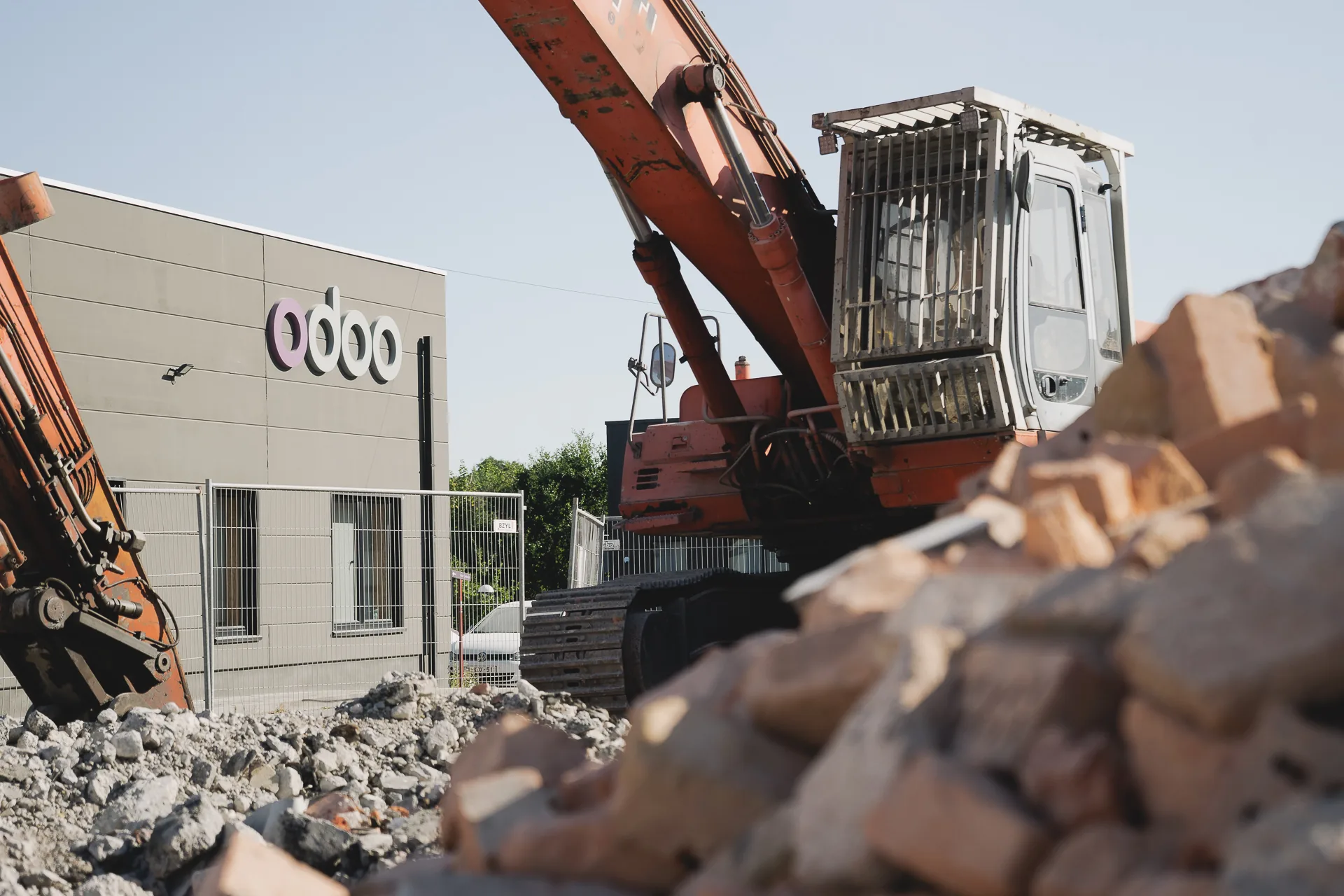 Une pelleteuse au pied du bâtiment Odoo, tas de briques déposées au premier plan