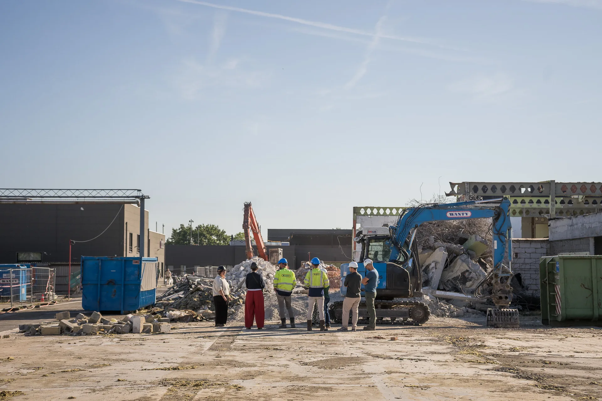 Vue large du chantier en déconstruction, un groupe de visiteurs au pied des engins