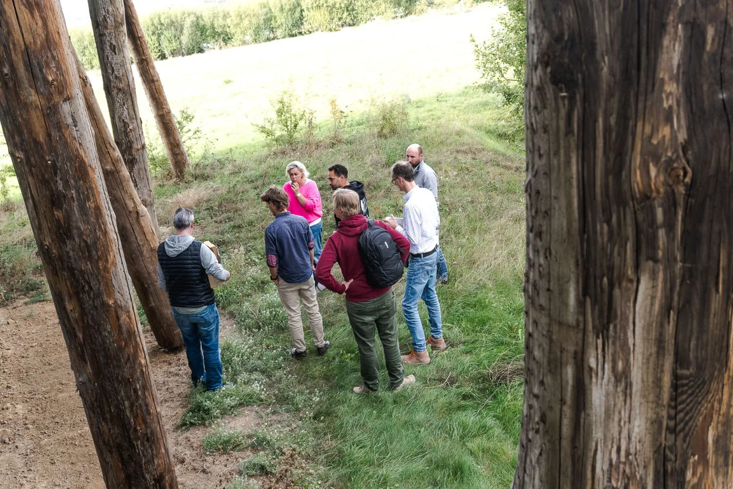 Le groupe au pied des pilotis en troncs bruts qui portent le bâtiment du Cluster Eco-construction