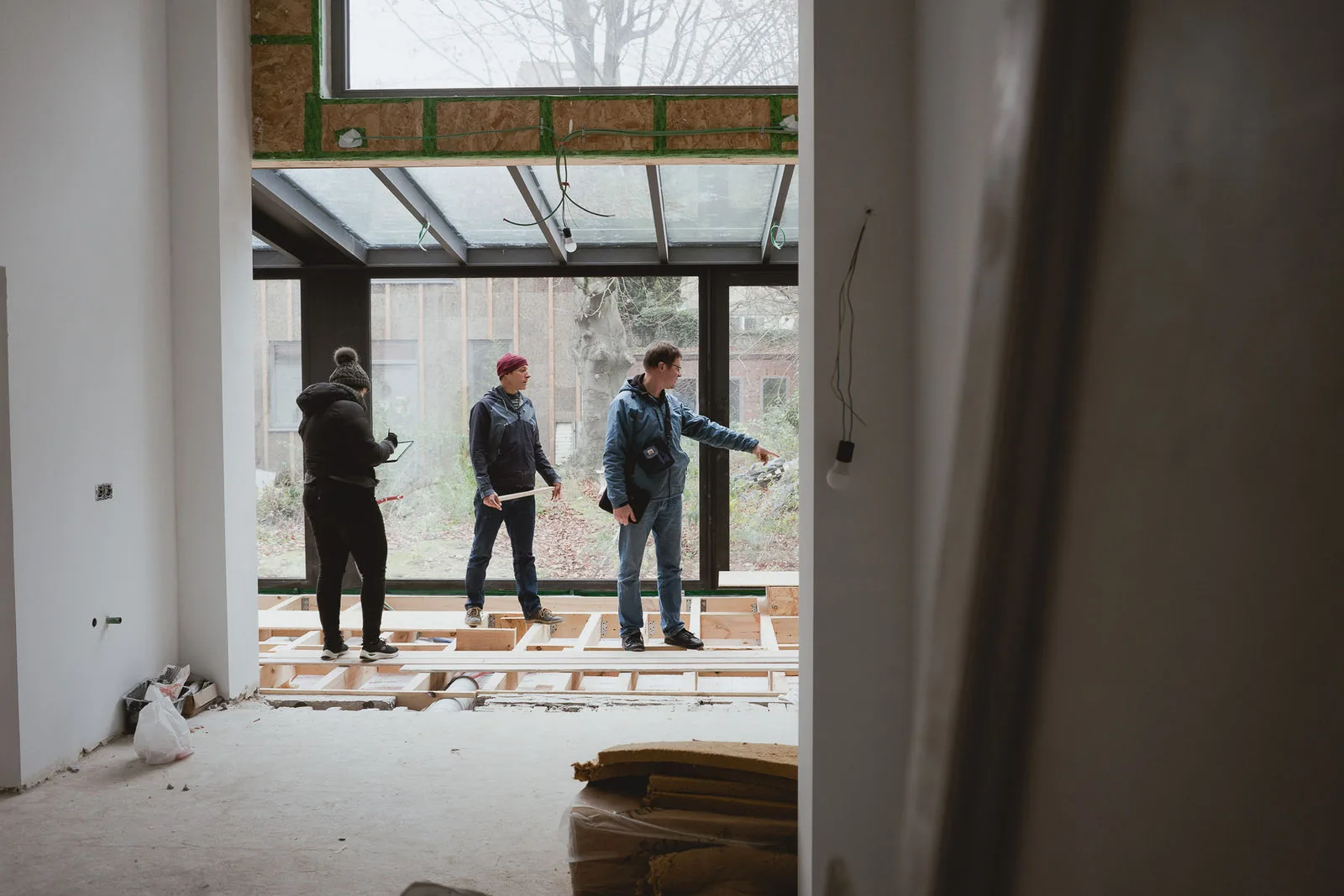 Visite de chantier : trois personnes dans la véranda, au-dessus du plancher en cours de pose
