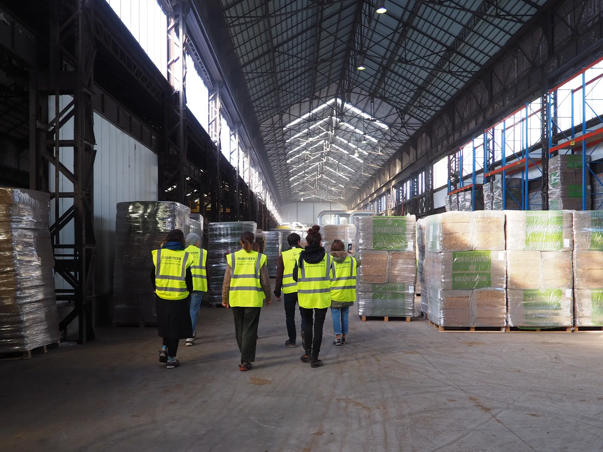 L'allée centrale de l'usine d'Auvelais, palettes d'isolant de part et d'autre, visiteurs en gilet