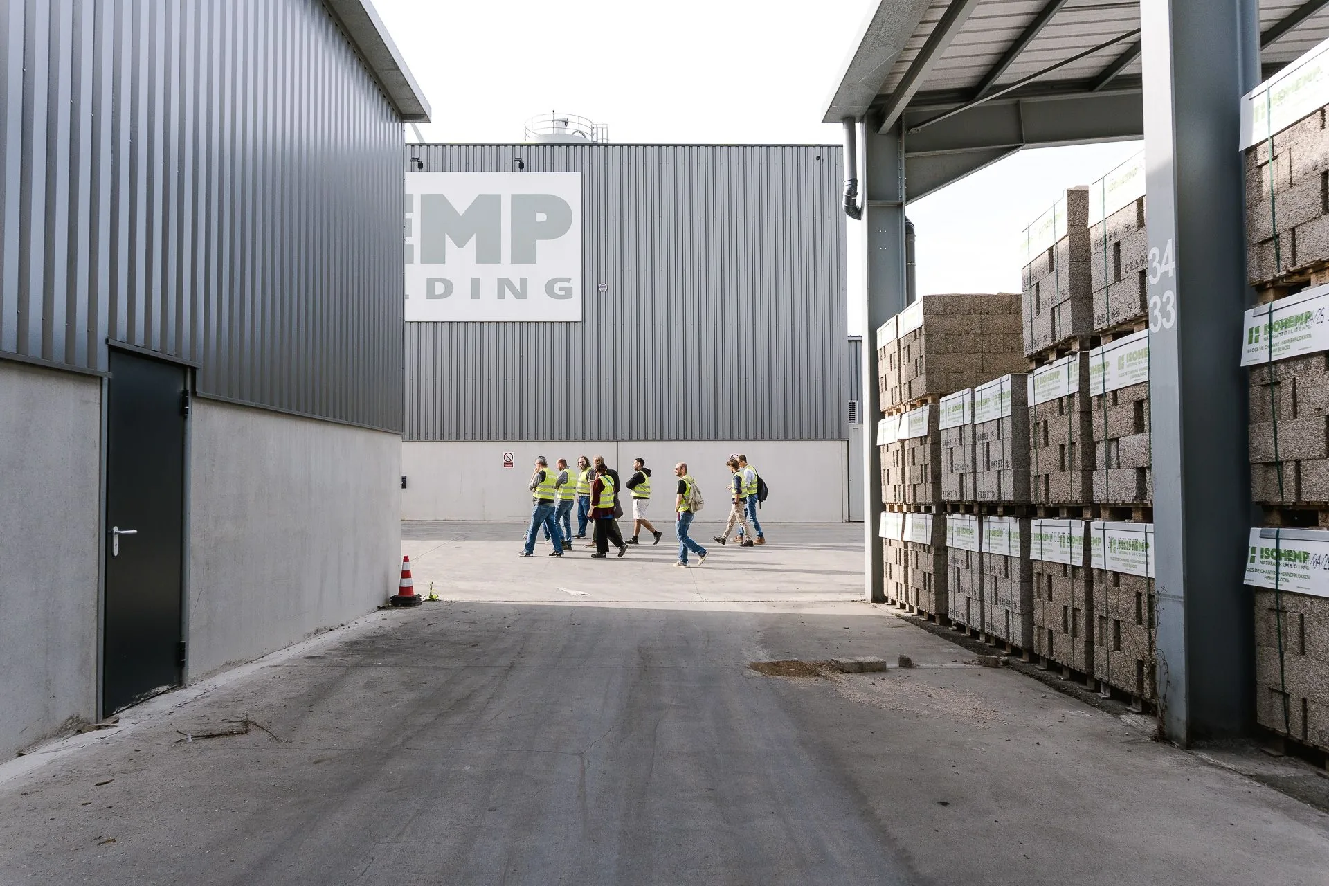 Les visiteurs traversent l'usine IsoHemp entre deux halls, les palettes de blocs en bordure