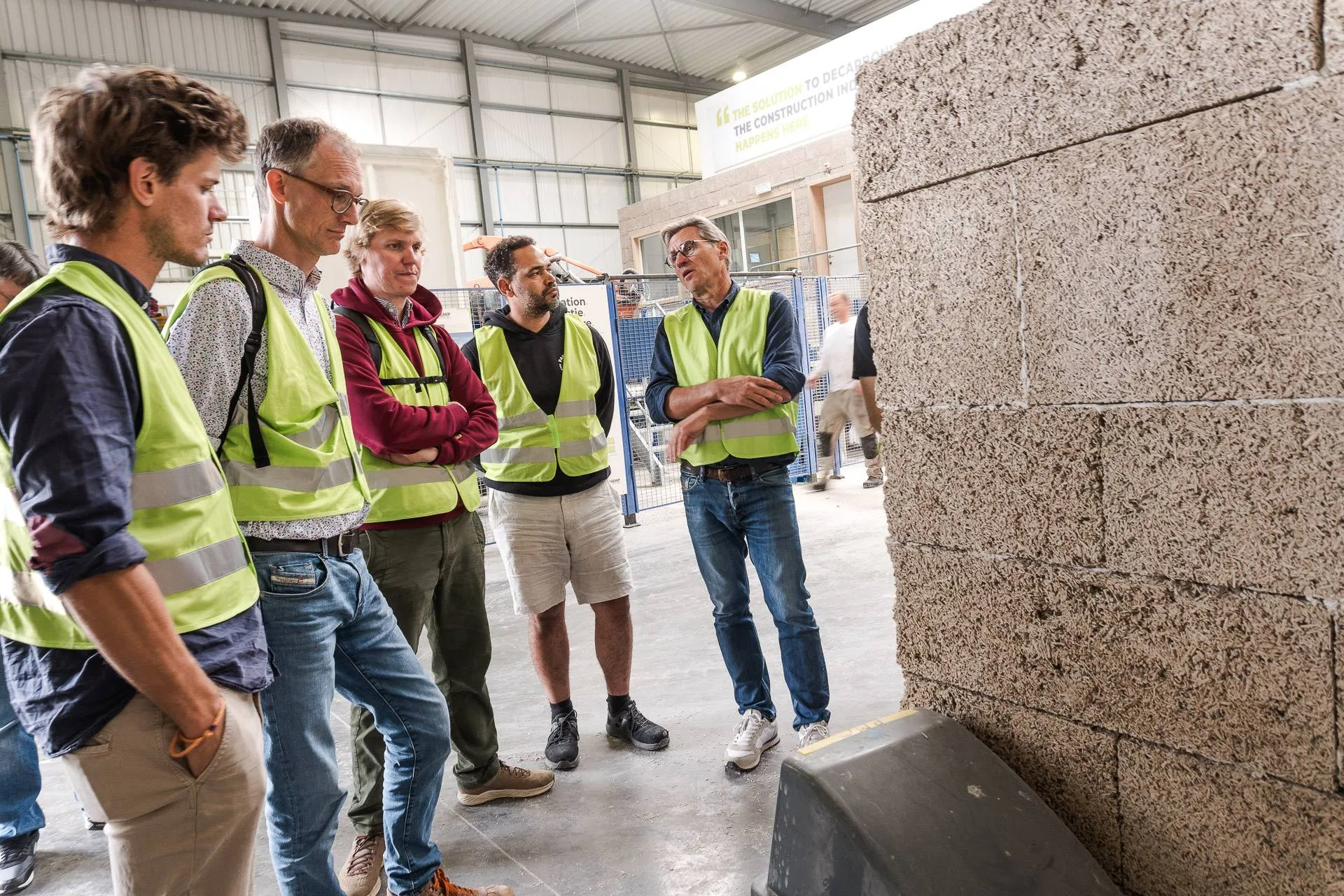Le groupe écoute le guide d'IsoHemp devant un mur en blocs de chanvre à Fernelmont