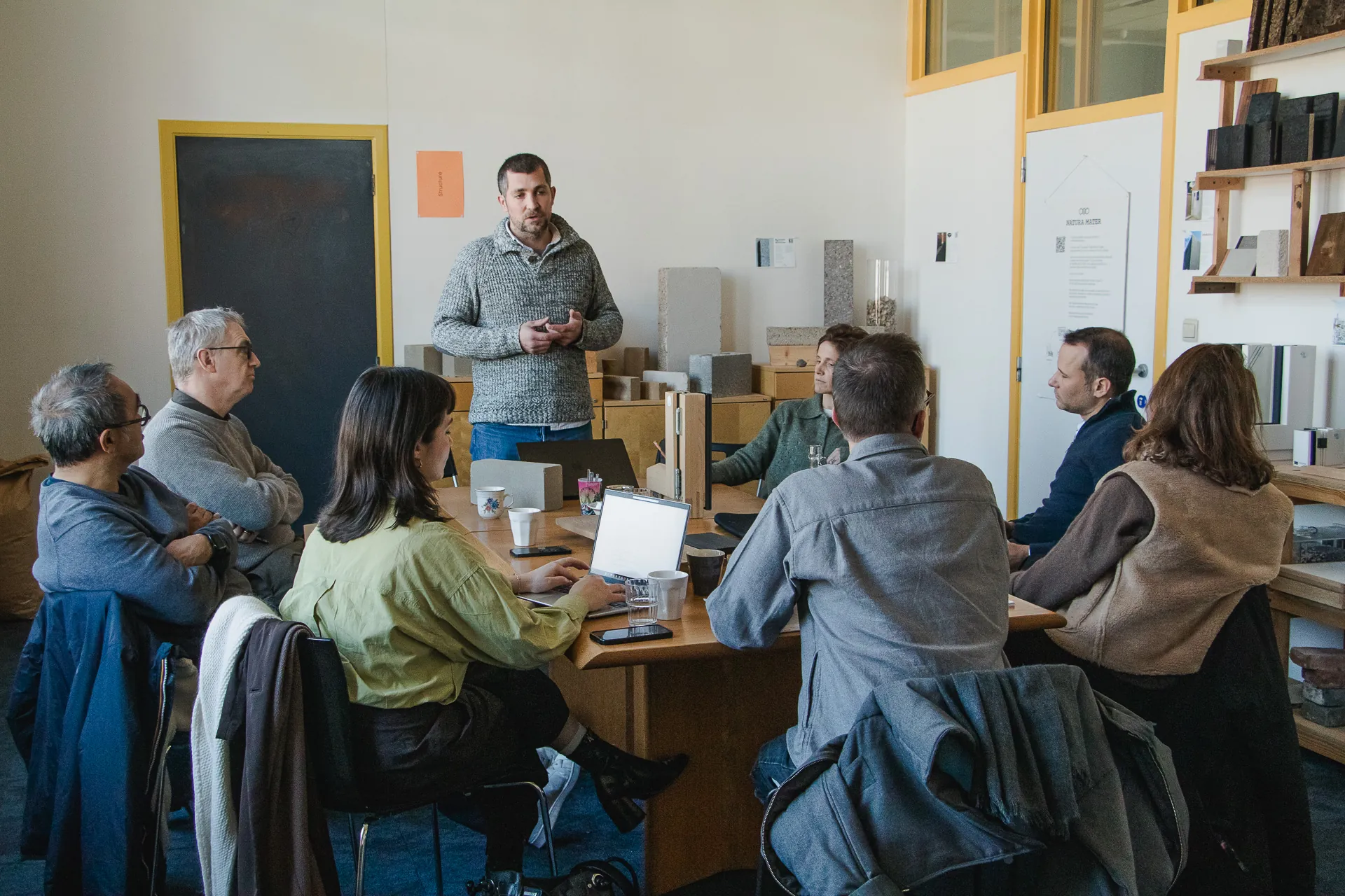 Un module de la Master Class en séance à la Materatek : l'intervenant debout, huit participants autour de la table, des blocs de matériau posés sur le bahut et la feuille « Structure » au mur