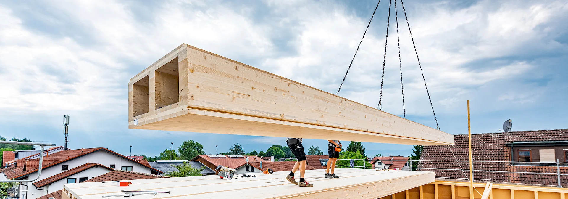 Élément CLT BOX levé à la grue au-dessus d'une toiture en cours de surélévation, ouvriers en attente — référence « Aufstockung im Holzbau ». Crédit dans le nom de fichier : © ingorack.com