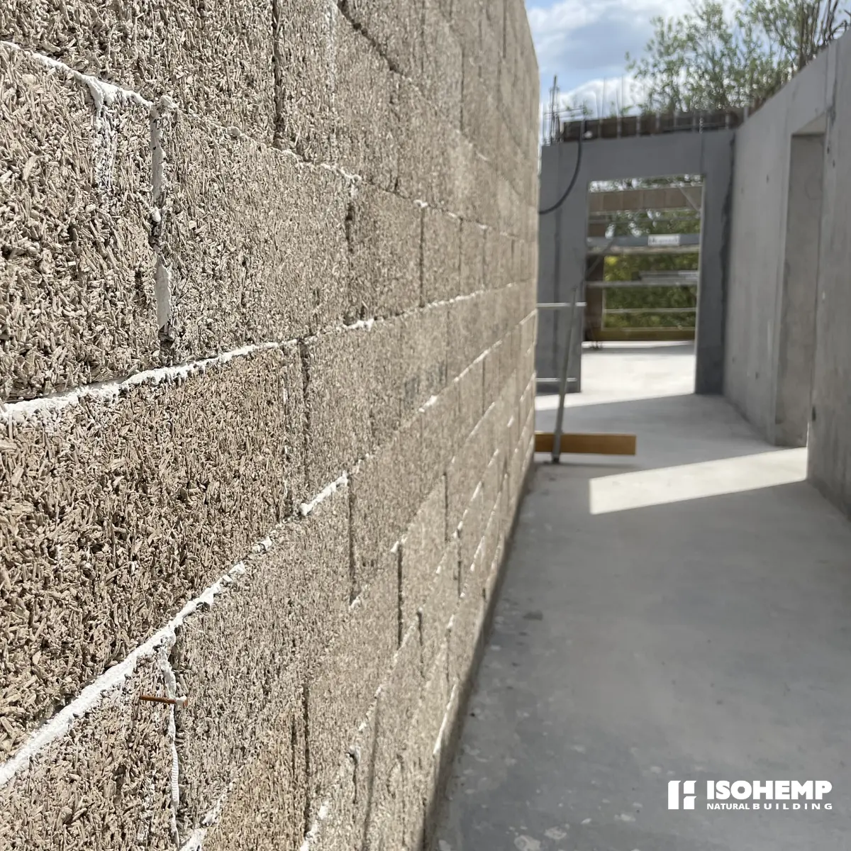 Mur de blocs de chanvre en lumiere rasante : texture chenevotte + liant chaux, joints minces, couleur reelle grise/beige