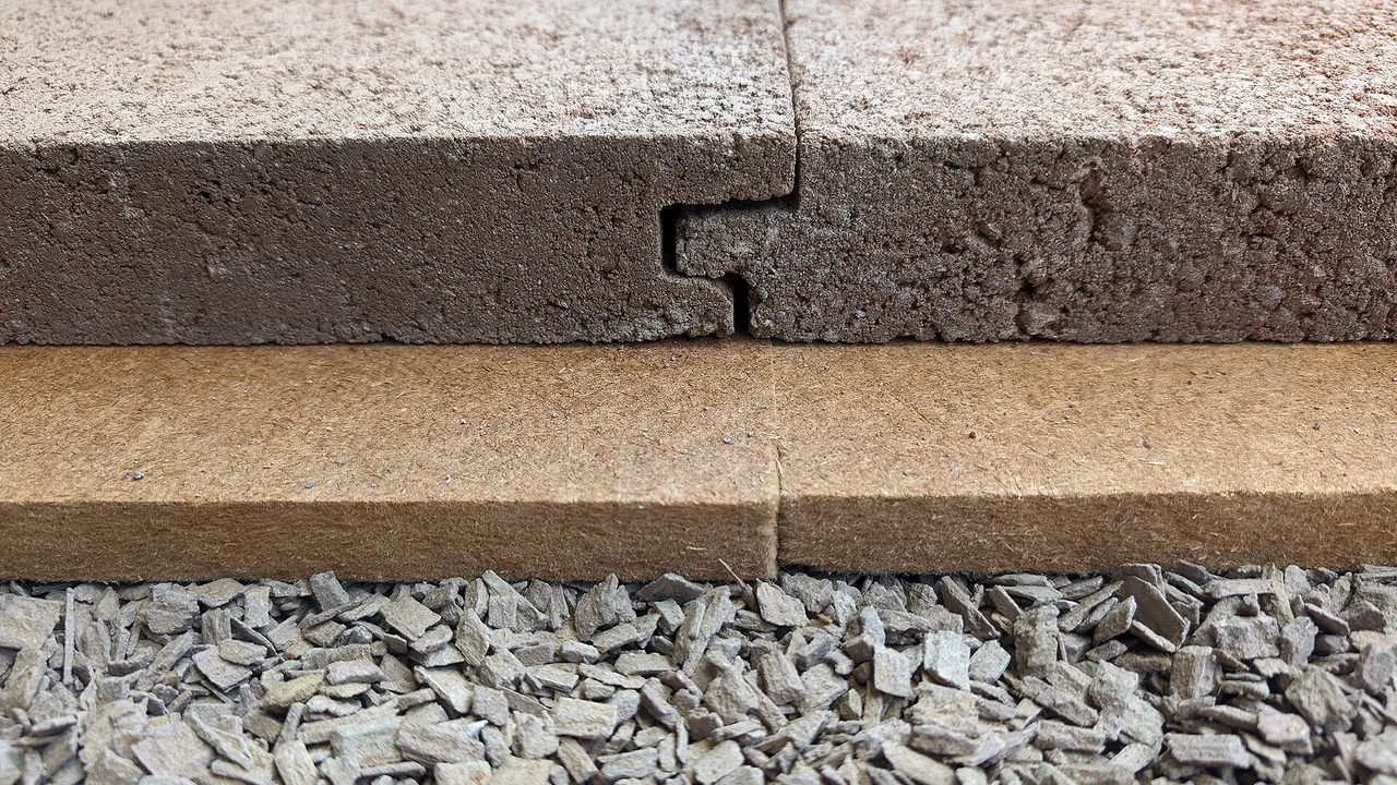 Coupe rapprochee du complexe de sol : herisson de gravier, panneau isolant, puis dalle Lithotherm avec son assemblage rainure-languette — grain du beton de lave en gros plan