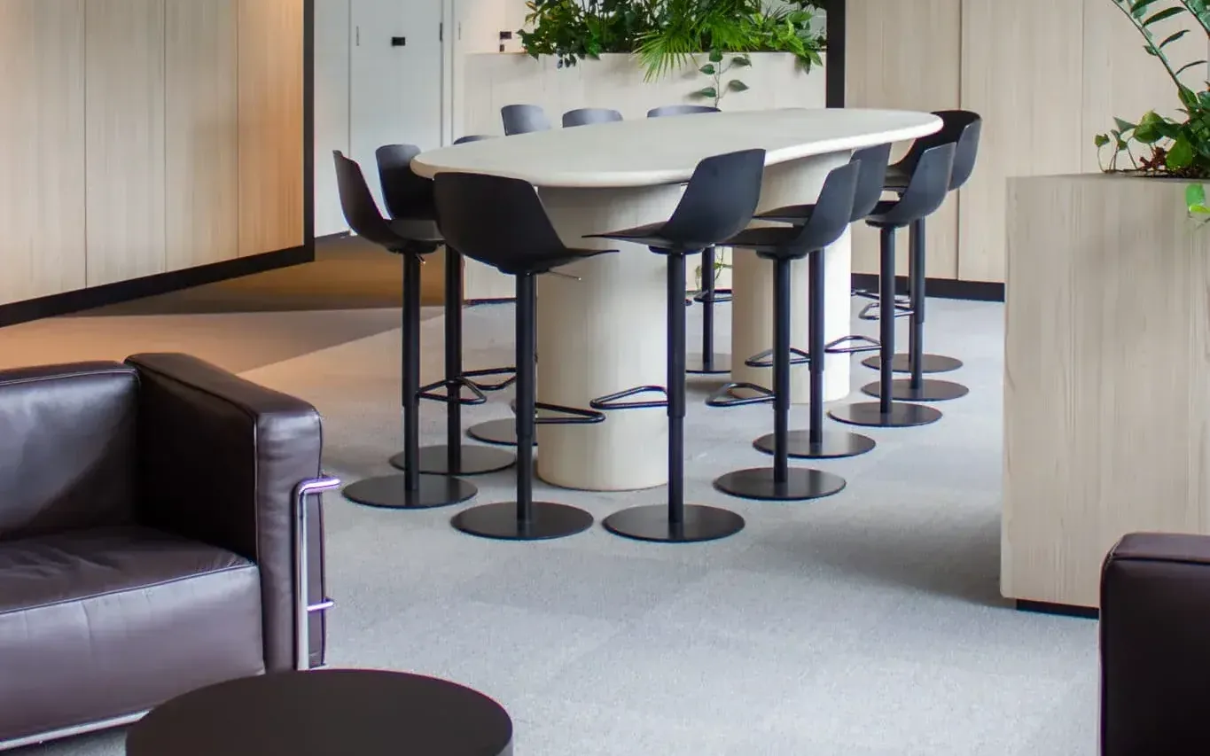 Office floor laid with beige reclaimed carpet tiles, around a high table