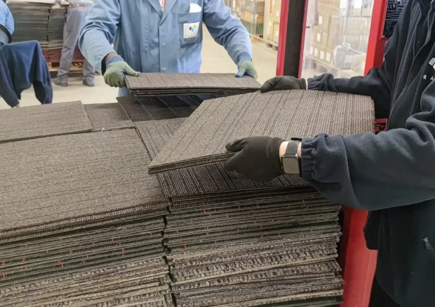 Two people stacking lifted carpet tiles during sorting