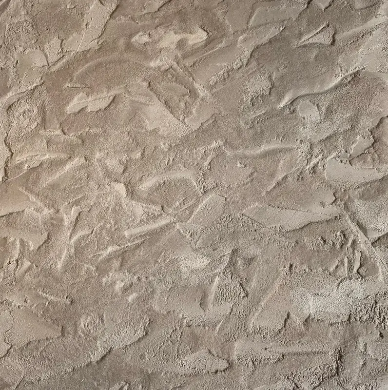 Gros plan sur une finition Claystone effet pierre naturelle (chantier Matonge, Bruxelles) : reliefs de lisseuse, plages lissées et arrachements, teinte sable/taupe en lumière rasante.