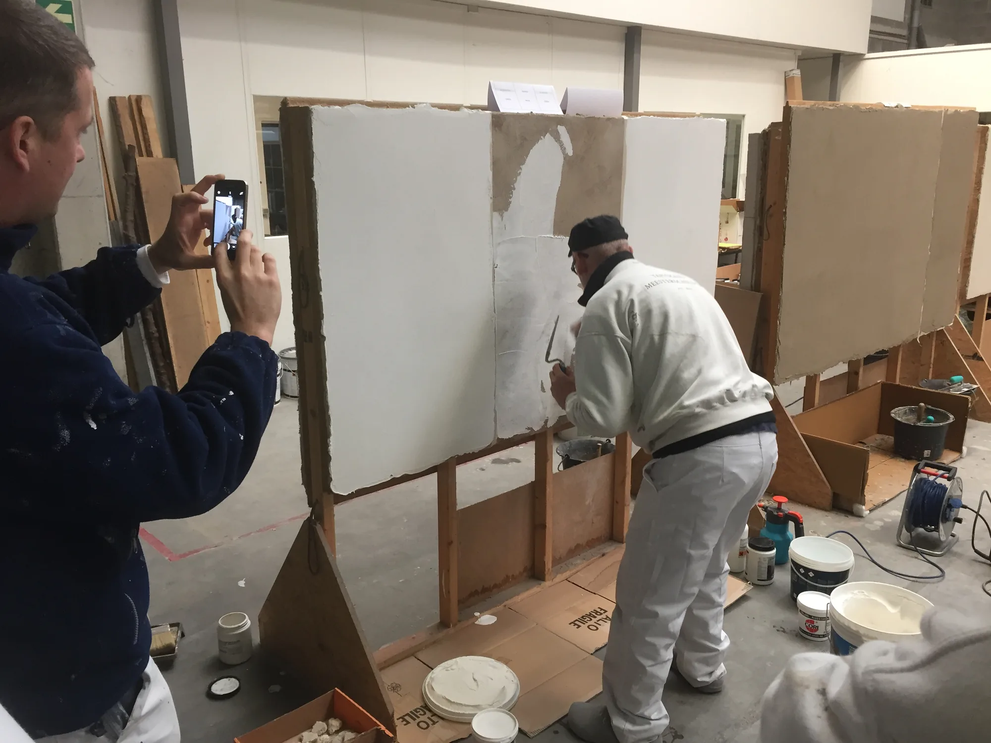Application et lissage à la truelle d'un enduit de finition à la chaux clair sur panneau d'essai, lors d'une session de démonstration Arte Constructo