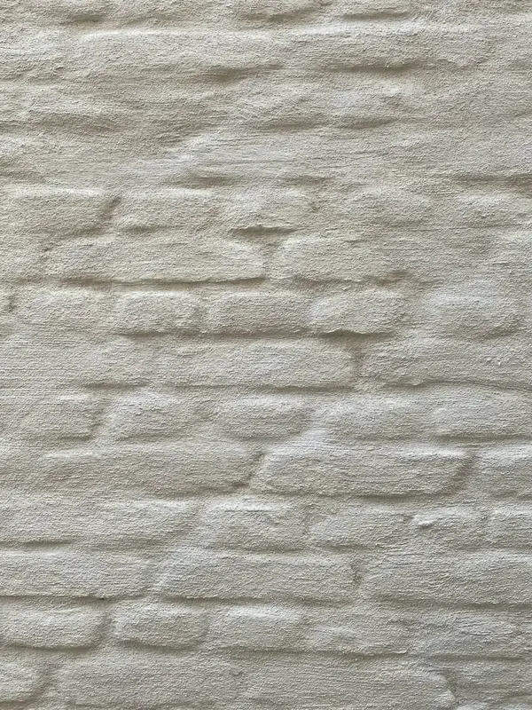 Enduit de finition à la chaux naturelle Unilit sur maçonnerie de brique, teinte blanc cassé légèrement grisée : pan de mur cadré serré et frontalement, sans ciel ni ouverture (maison privée à Wingene-Zwevezele)