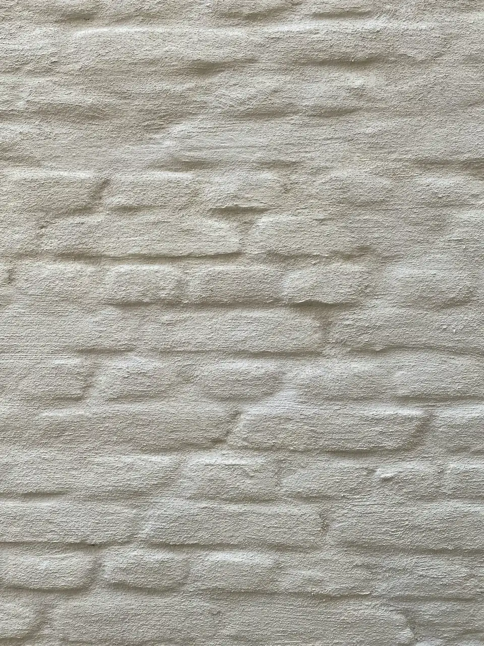 Enduit de finition à la chaux naturelle Unilit sur maçonnerie de brique, teinte blanc cassé légèrement grisée : pan de mur cadré serré et frontalement, sans ciel ni ouverture (maison privée à Wingene-Zwevezele)