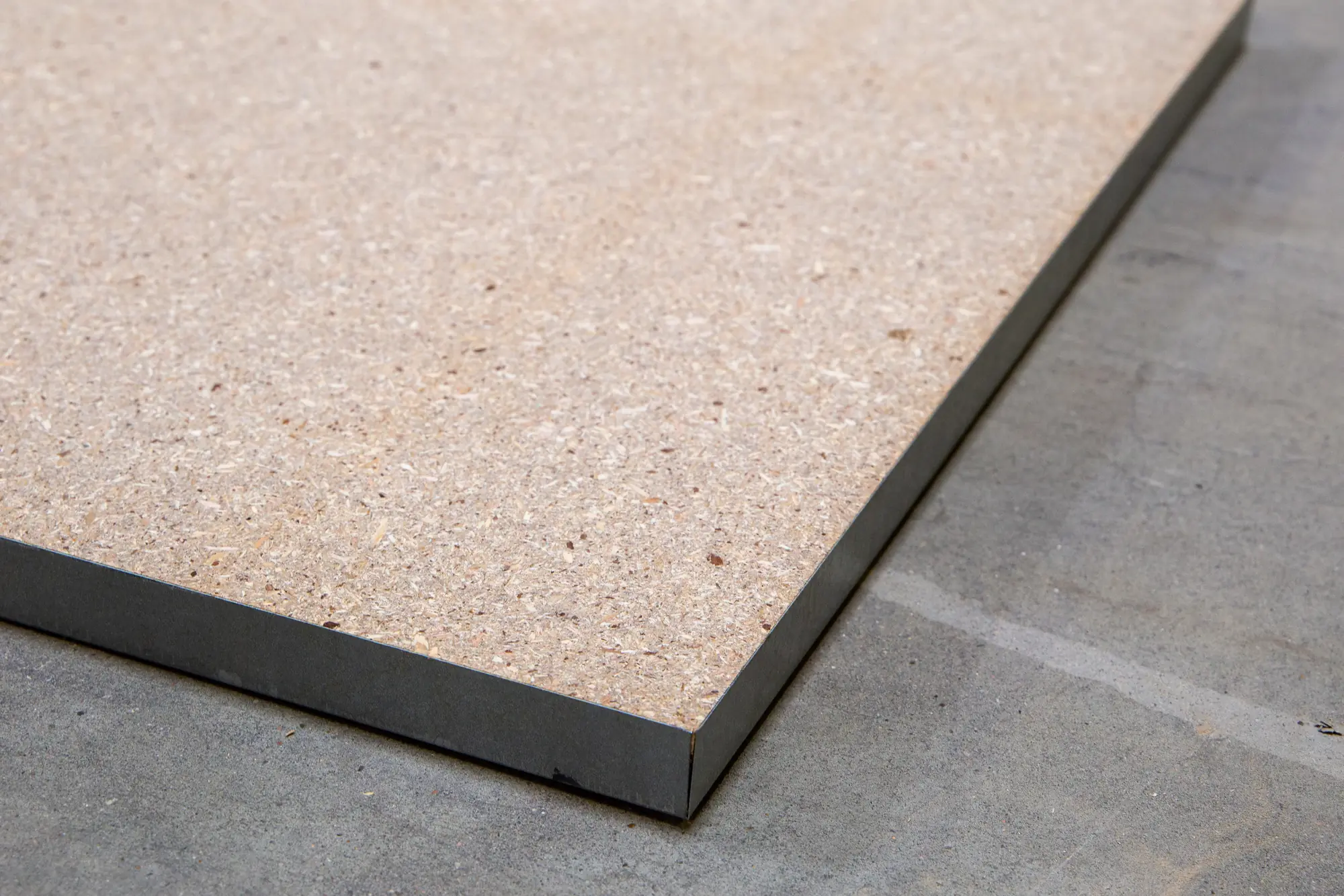 Dall'R30B - dalle de plancher technique de réemploi, âme en panneau de particules haute densité, angle et chant apparents, posée sur béton (fond neutre gris)