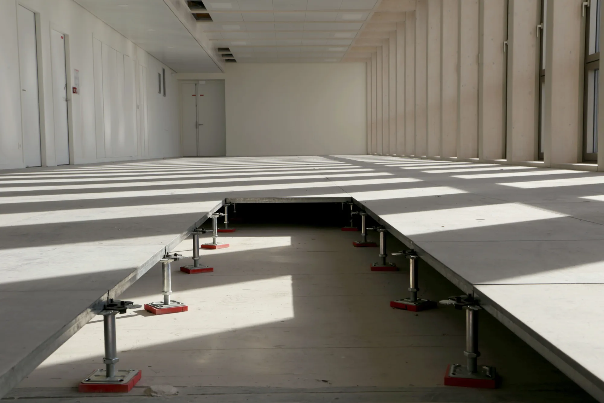 Montage du plancher technique en cours : dalles posées sur plots réglables, une dalle retirée laissant voir le vérin et le plénum
