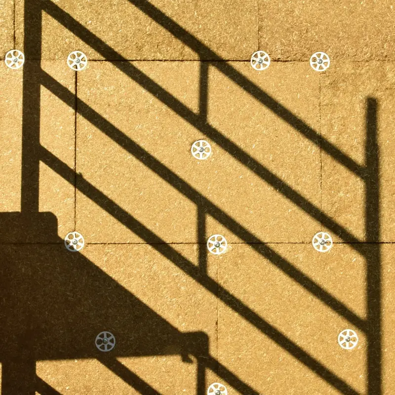 Gros plan sur la façade isolée : grain et couleur réelle de la paille compressée, joints entre panneaux et rosaces de fixation