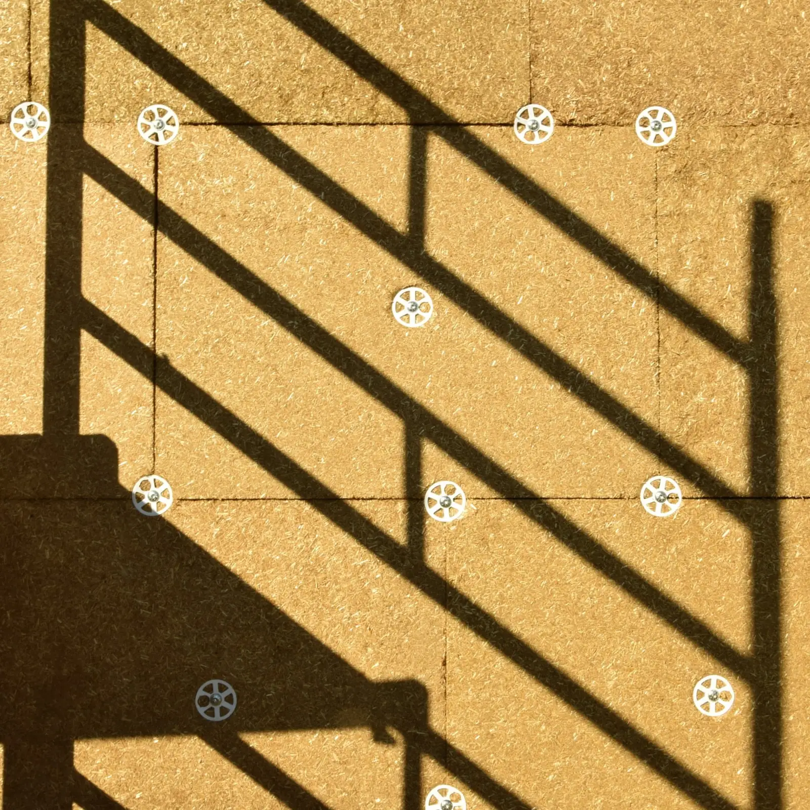 Gros plan sur la façade isolée : grain et couleur réelle de la paille compressée, joints entre panneaux et rosaces de fixation