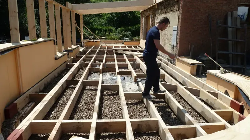 Chantier : lit de coquillages sur terre-plein sous solivage bois, ouvrier au travail — vue large horizontale