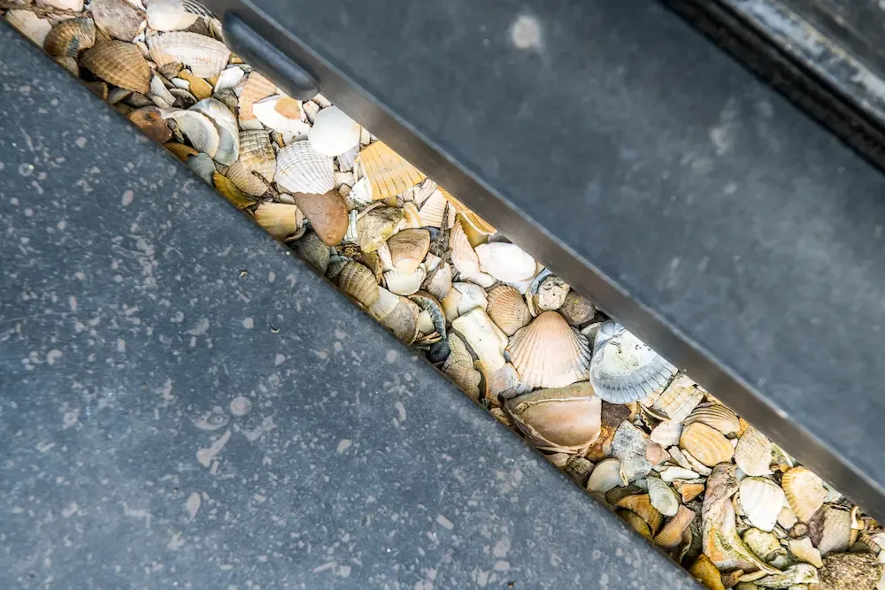 Coquillages Ecoschelp dans la goulotte de la souffleuse — cadrage serré sur le matériau seul, coquilles entières bien lisibles