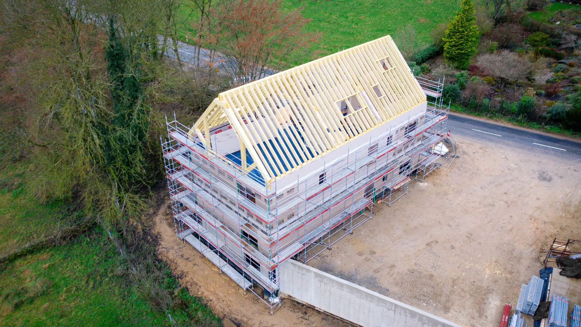 Aerial view of a timber house under construction, surrounded by scaffolding, roof structure in place
