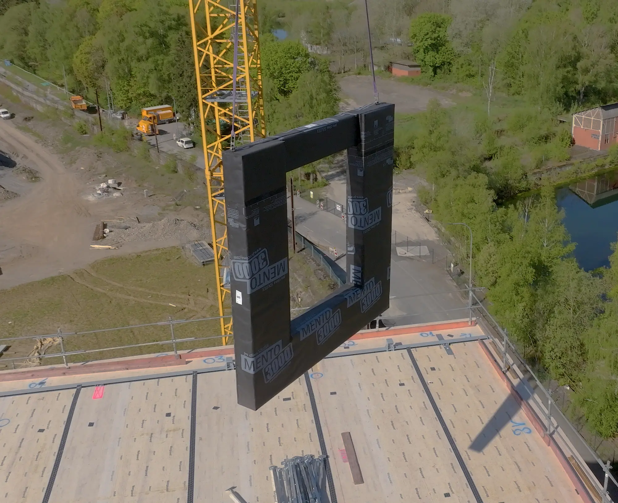 Prefabricated wall element with its window opening, lifted by crane above a floor