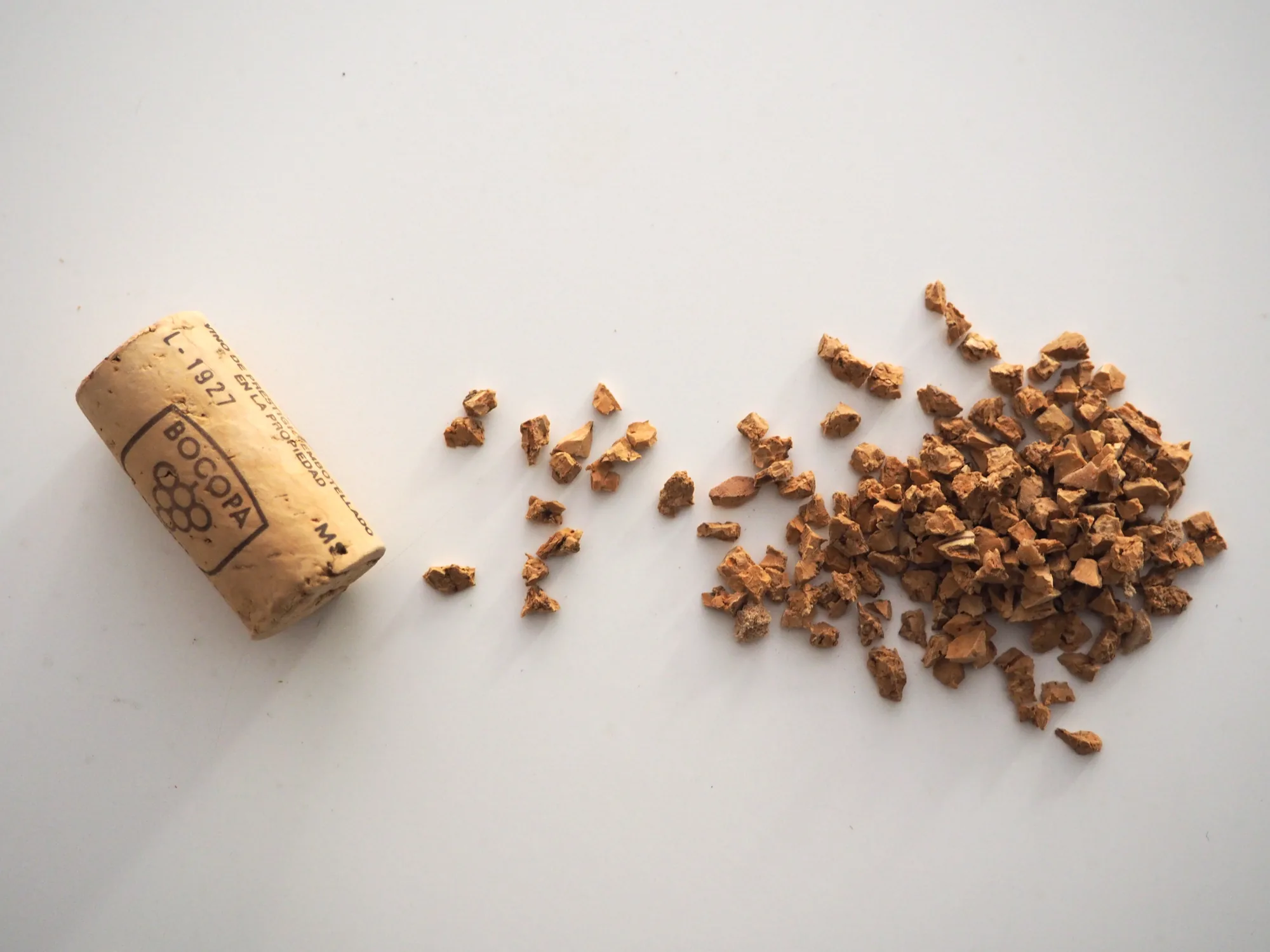 Bouchon de liège usagé et granulés de liège recyclé (deux granulométries) posés sur fond blanc neutre - le produit et sa matière première
