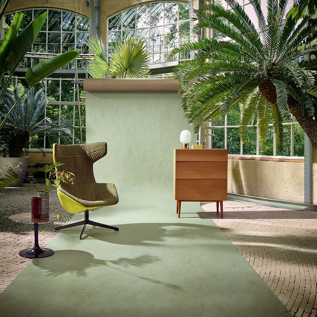 Sol en linoléum vert dans une véranda plantée, fauteuil et enfilade