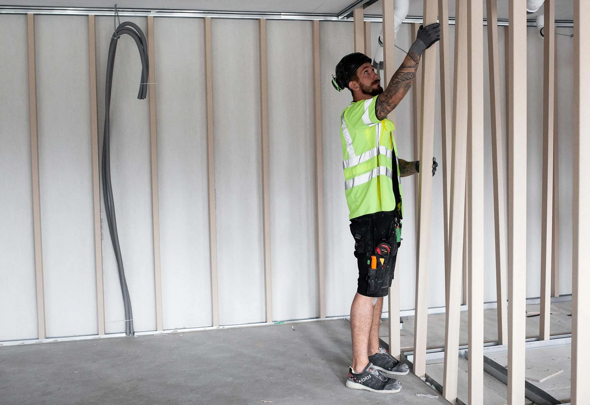 Pose de montants Wood Tube sur un mur de chantier, vue large de l'ouvrier au travail